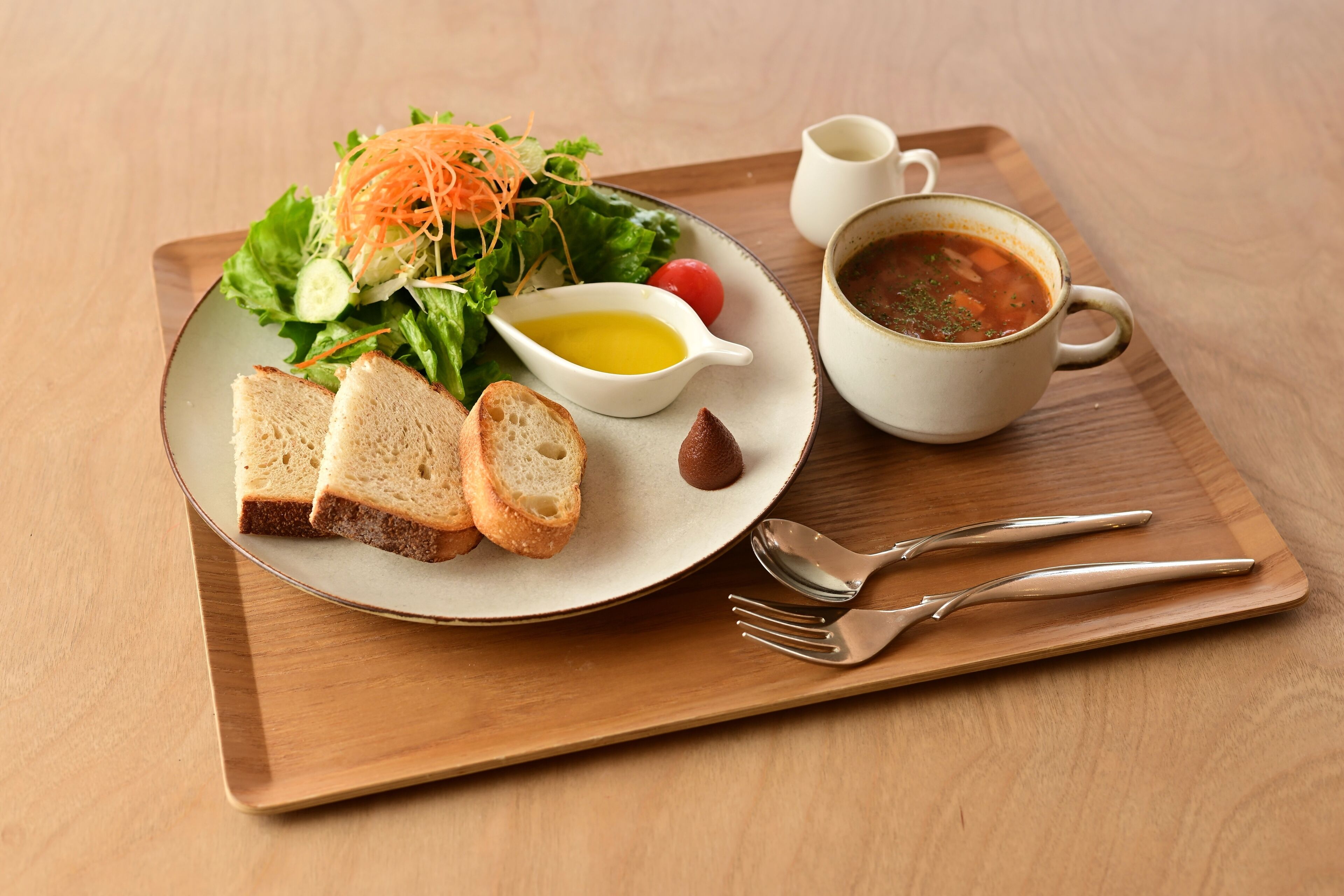 A plate with a salad, bread, and a soup cup on a wooden tray.