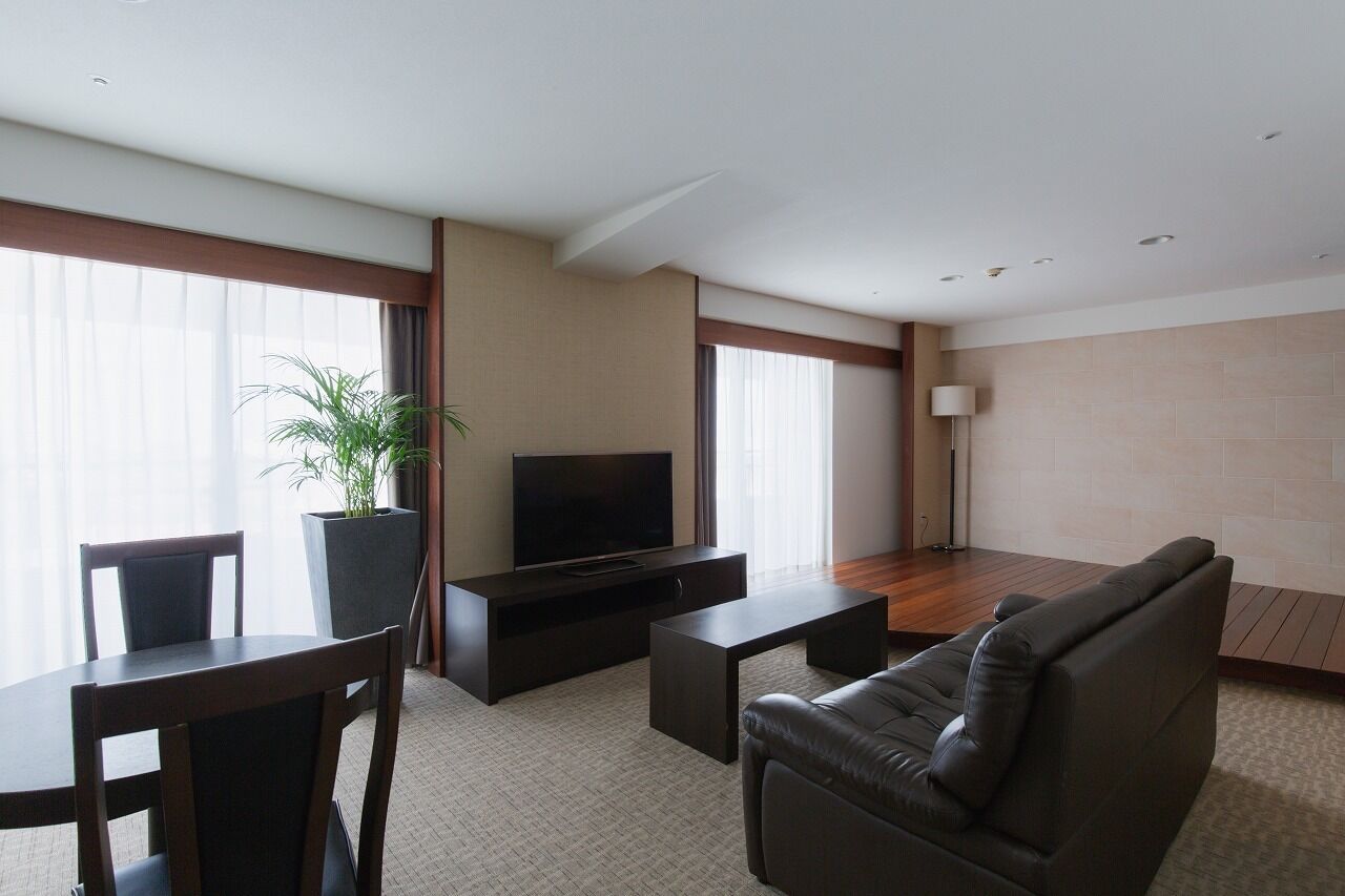 A modern living room with a sofa, a TV, a dining table, and a potted plant.