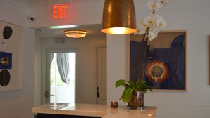 A reception area with a marble counter, a vase with orchids, a painting, and an exit sign.
