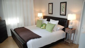 A neatly made bed with a brown throw blanket, two bedside lamps, and green patterned pillows.