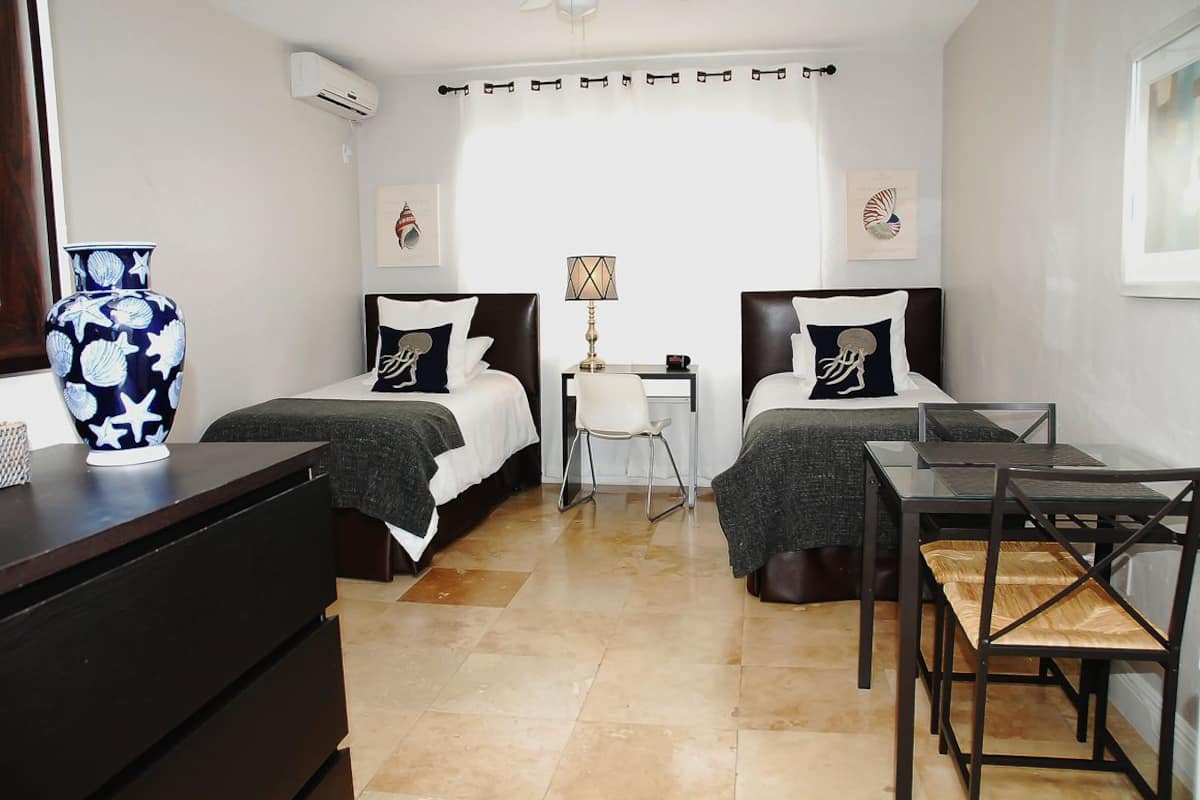 A bedroom with two beds, a desk, a chair, a lamp, and a large vase.