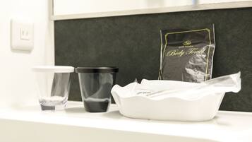 Una encimera de baño con un lavabo blanco, una taza negra, un recipiente blanco y un paquete que dice "Soft Touch Body Towel".