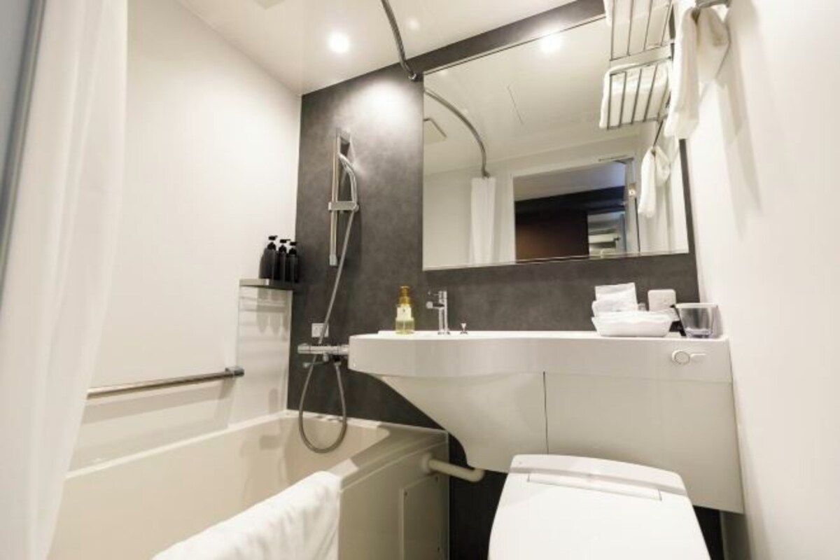 Uma casa de banho moderna com lavatório branco, espelho e chuveiro.