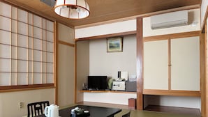 Una habitación tradicional japonesa con suelo de tatami, una mesa baja con un hervidor y teteras, un televisor y un armario.