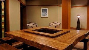 Una mesa de conferencias de madera con una sección central hundida, flanqueada por dos sillas, en una sala con paneles de madera y un cuadro en la pared.