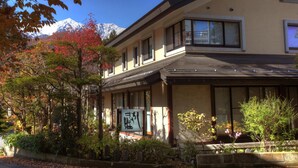 Un edificio japonés tradicional con un letrero, rodeado de follaje otoñal y un paisaje de montañas.