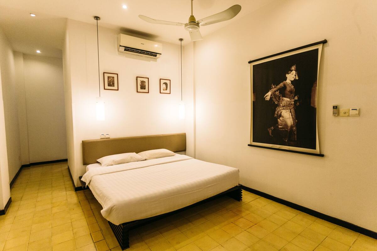 Una habitación de hotel con cama, ventilador de techo, aire acondicionado y un cuadro en la pared.