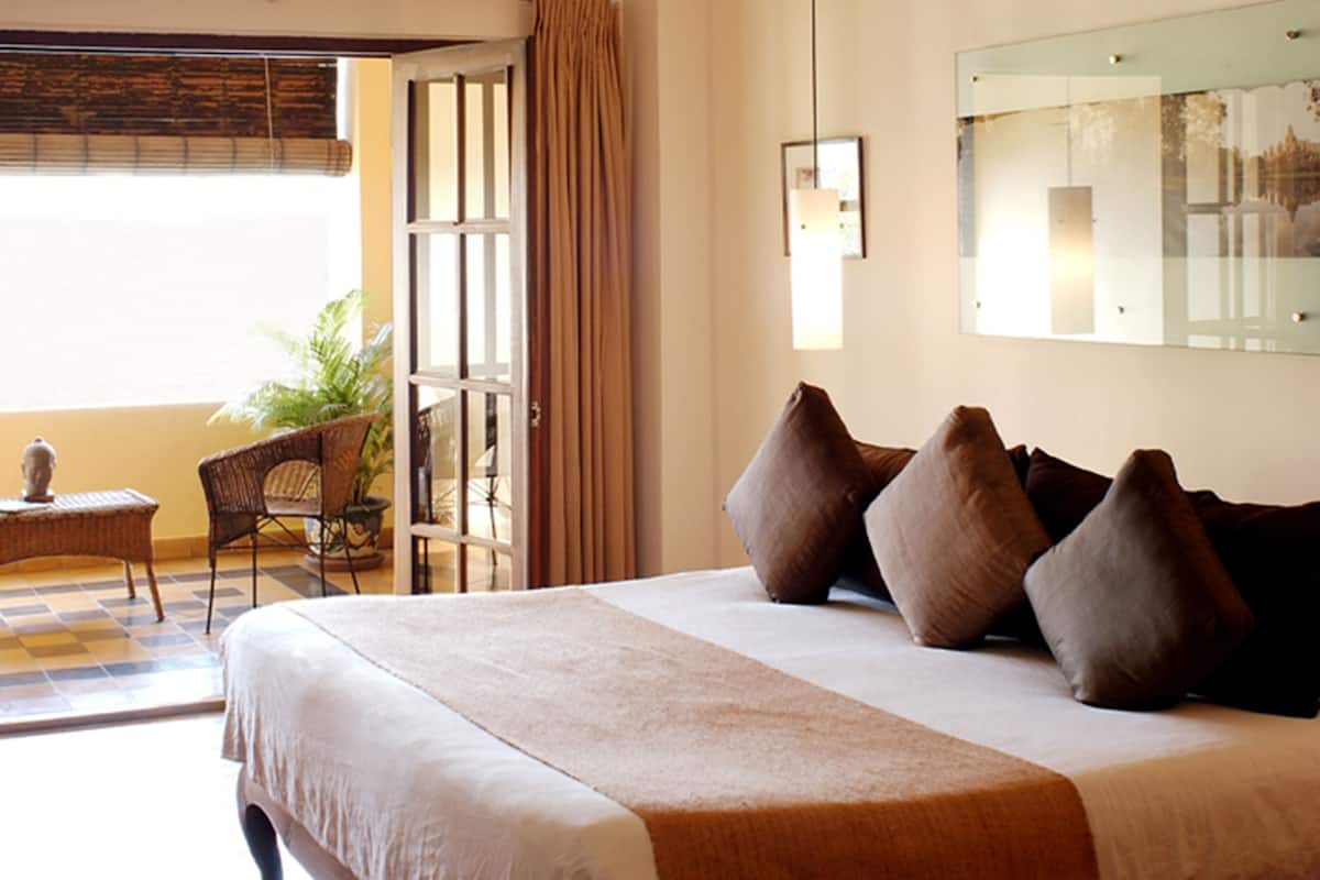 Habitación de hotel con una cama grande, una silla, una mesita y una planta en maceta.