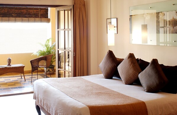 A hotel room with a large bed, a chair, a small table, and a potted plant.