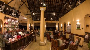 Een bar met een hoge plafond, houten stoelen en een toog met diverse flessen.