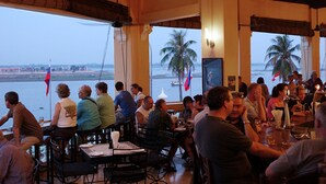 Een restaurant met tafels en stoelen, grote ramen en uitzicht op het water.