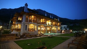 Un hotel grande de varios pisos con fachada de piedra, varios balcones y una piscina en el patio.