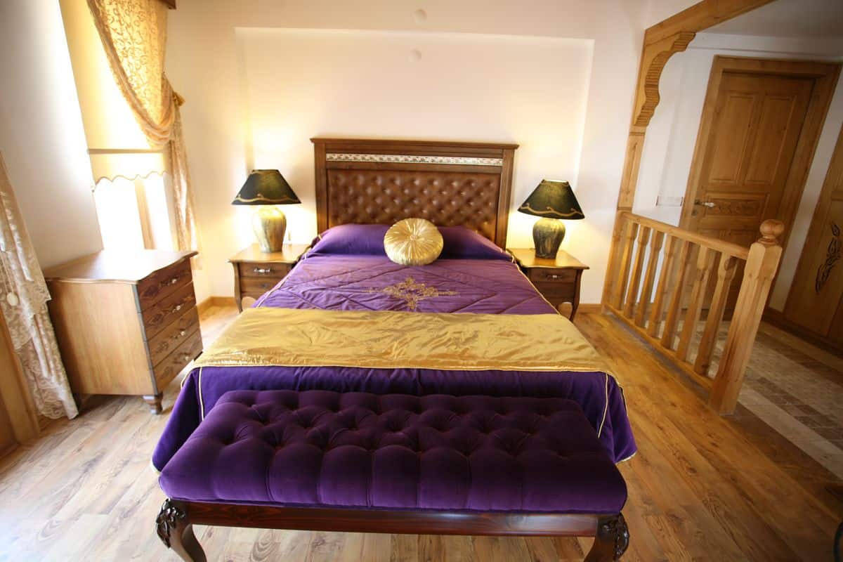 Quarto com uma cama grande, duas mesas de cabeceira com abajures, um painel de cabeceira de madeira e uma porta de madeira.