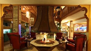 Un vestíbulo con una chimenea central, sillas tapizadas en rojo y una escalera de madera.