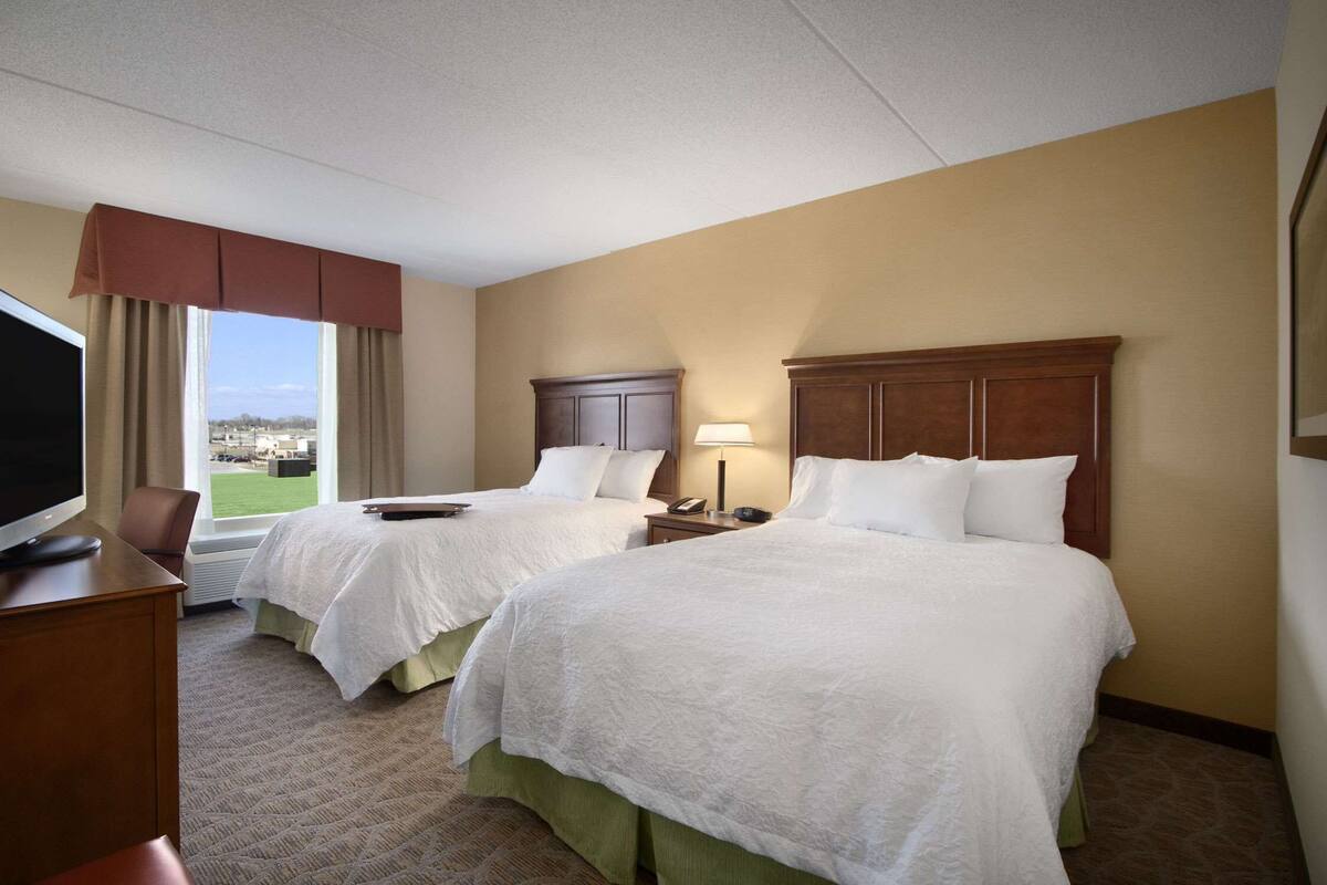A hotel room with two beds, a desk with a TV, and a window with a view of the city.