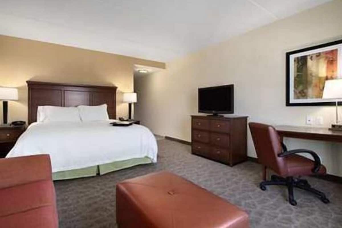 A hotel room with a bed, a desk with a chair, a television, and a painting on the wall.
