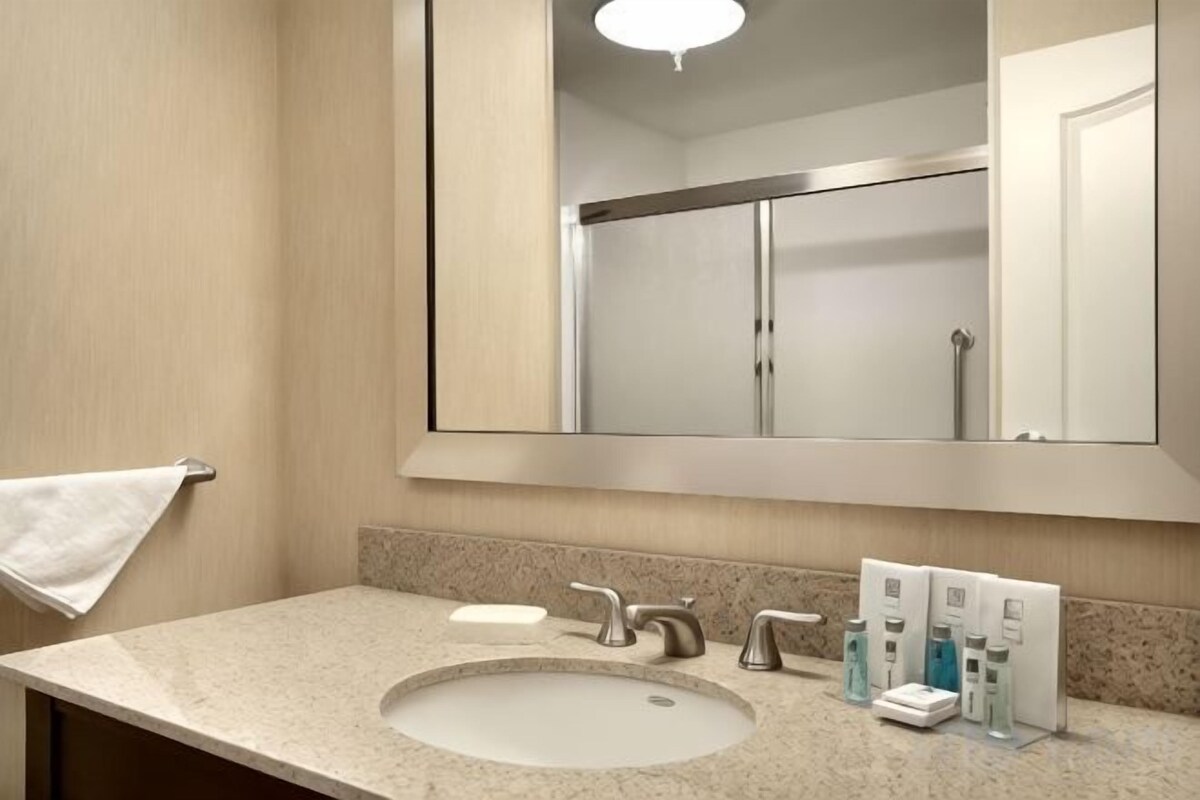 A bathroom with a sink, mirror, towel rack, and toiletries.