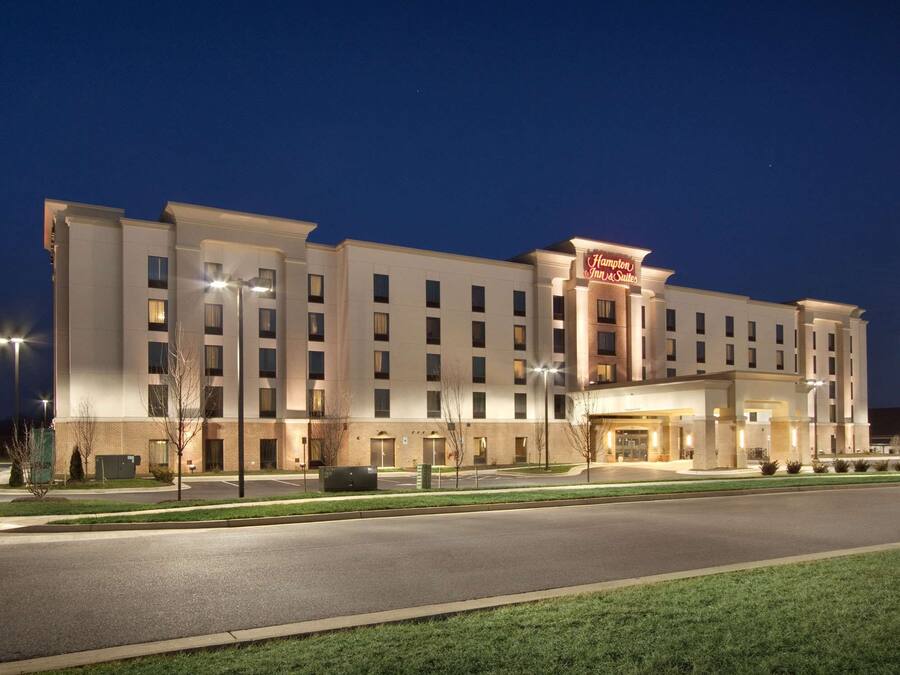 A multi-story hotel with a prominent 'Hampton Inn & Suites' sign, featuring a modern design with a flat roof and a large entrance.