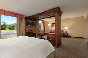 A hotel room with a large bed, a desk with a chair, a TV, and a view of the outdoors. - Hampton Inn & Suites Charles Town (Charles Town)