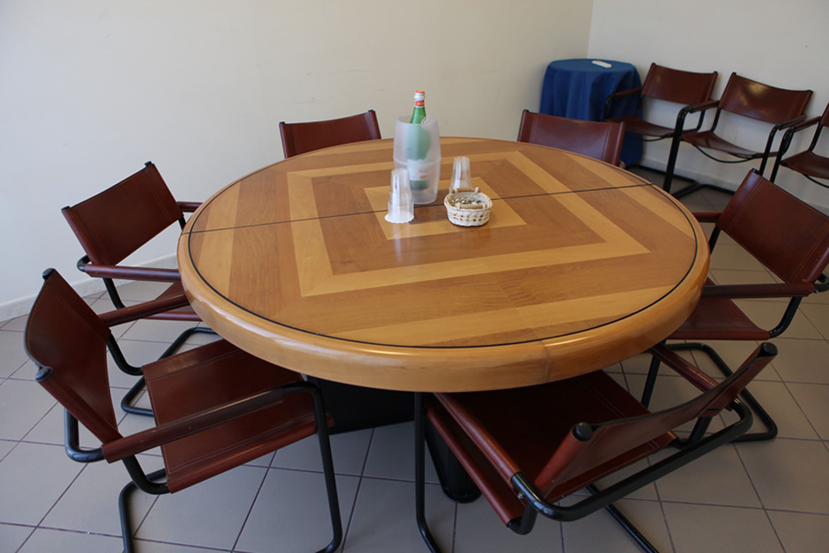 Ein runder Holztisch mit Glasplatte, umgeben von sechs braunen Stühlen mit Metallgestellen.
