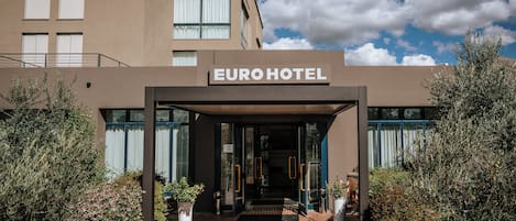 La entrada del Hotel Euro, con un diseño moderno, cuenta con un acceso despejado, plantas en macetas y un camino de ladrillo.