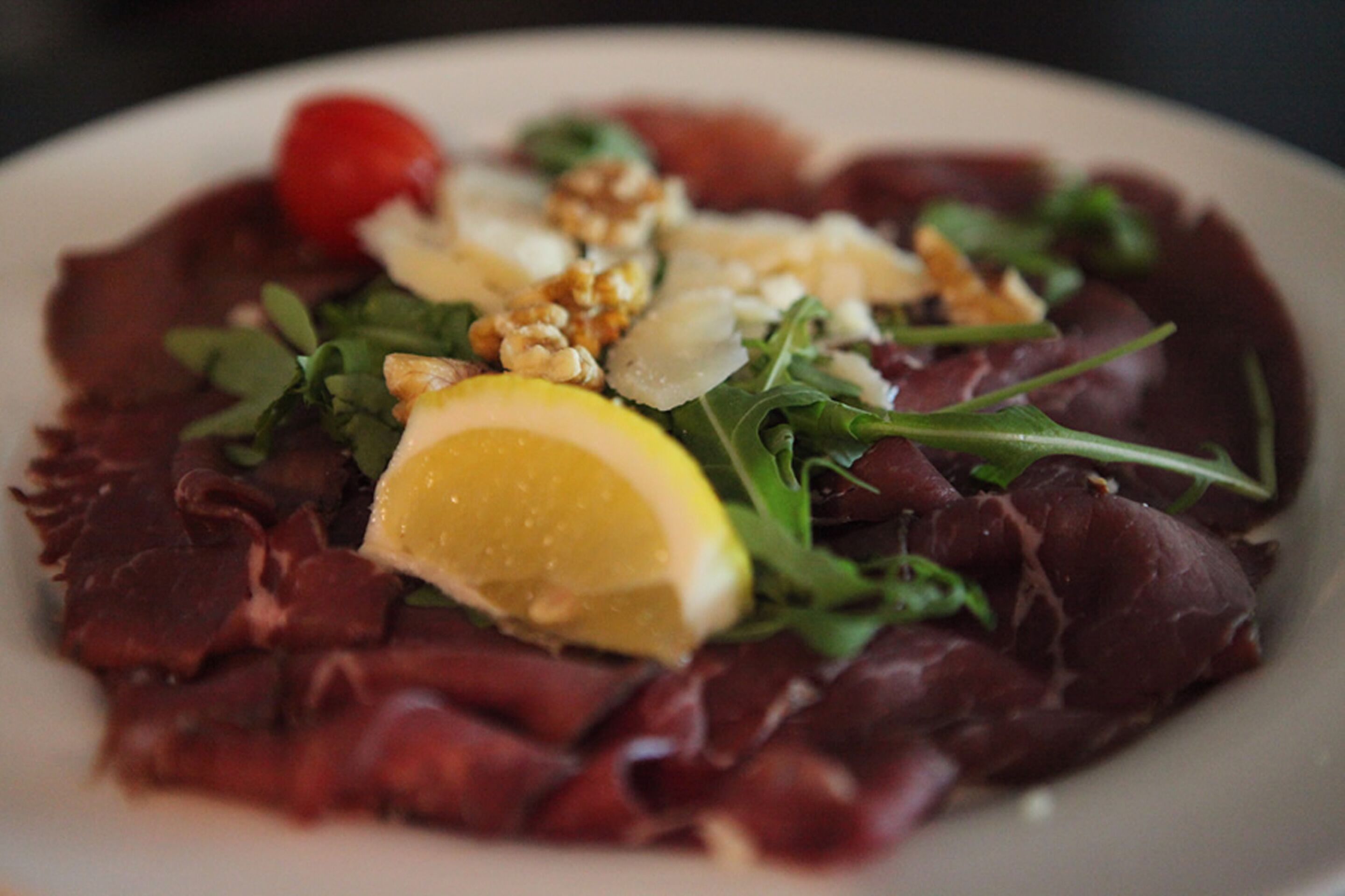 A plate of food with red meat, greens, nuts, and a lemon slice.