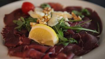 Une assiette de nourriture comprenant de la viande rouge, des légumes verts, des noix et une tranche de citron.