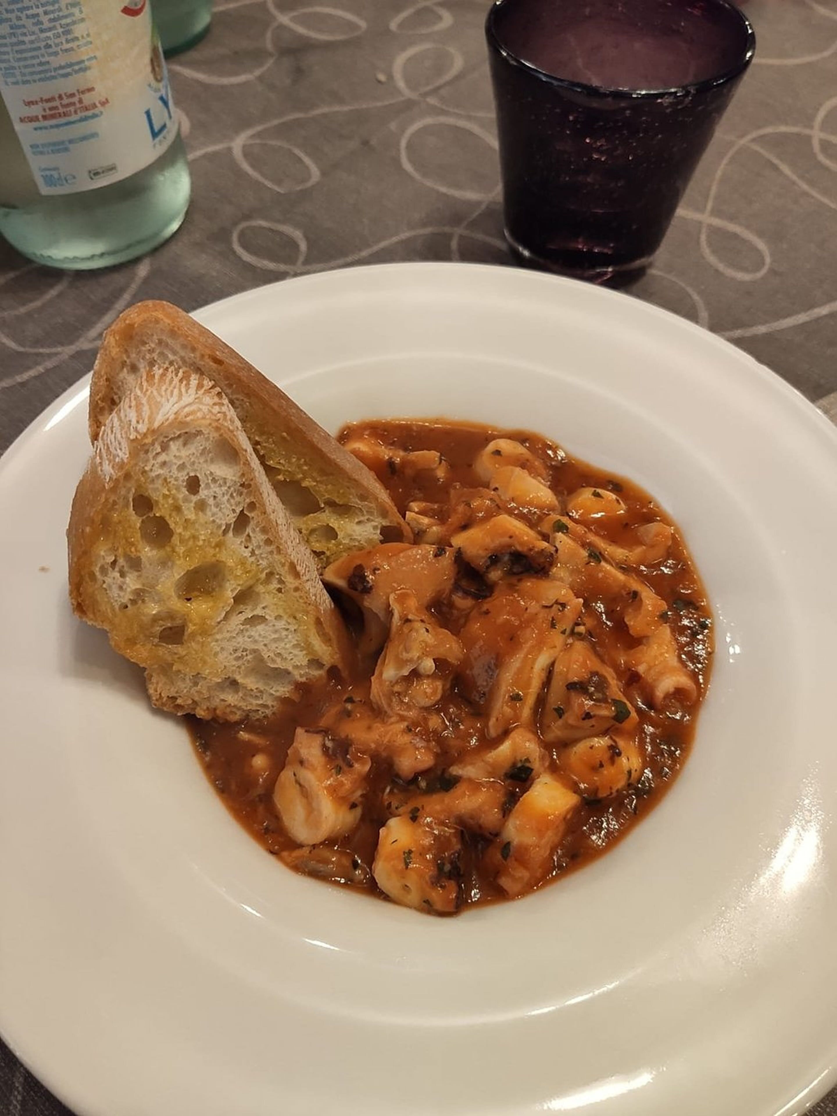 A plate of seafood stew with bread on a table.