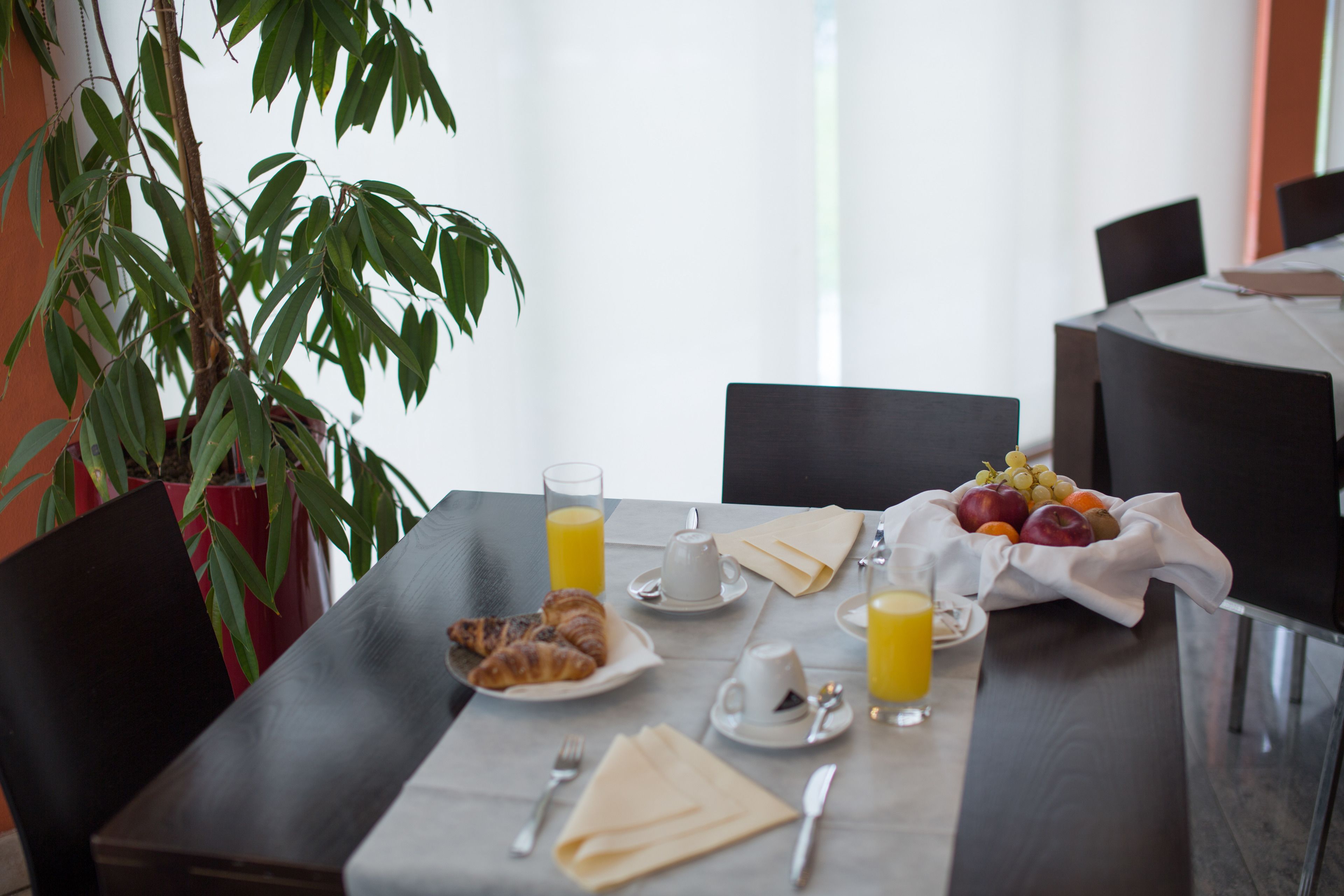 Ein Esstisch mit Croissants, Obst, Saft und einer Topfpflanze.