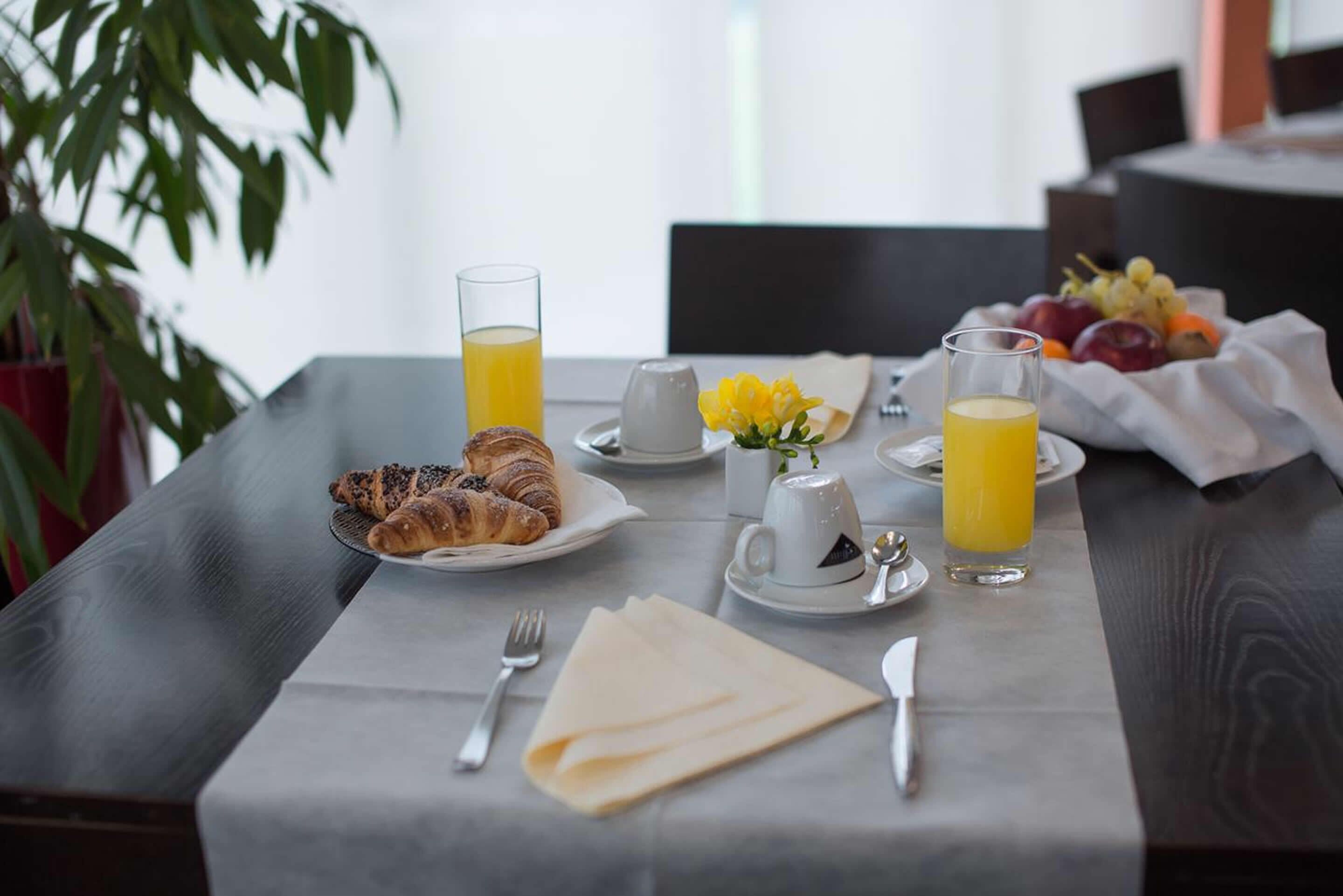 A breakfast setting with croissants, orange juice, and a fruit bowl on a table.