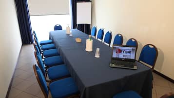 A conference room with a long table, blue chairs, a laptop, a whiteboard, and a projector screen.
