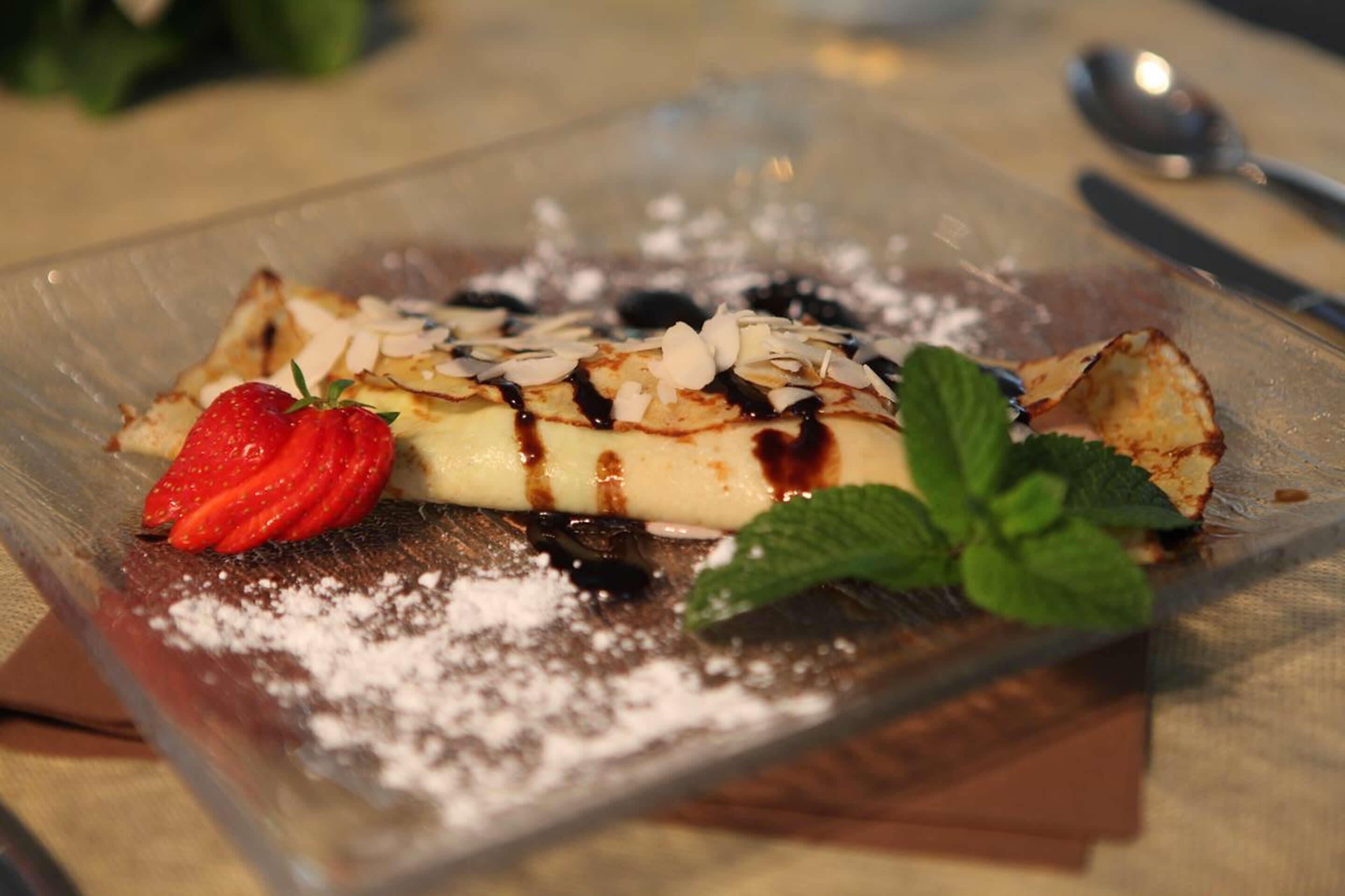 A dessert on a clear glass plate with powdered sugar, a strawberry, and mint leaves.