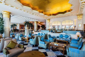 A spacious lobby with striped seating, a checkered floor, and a grand staircase. - Corniche Hotel Sharjah (Sharjah)