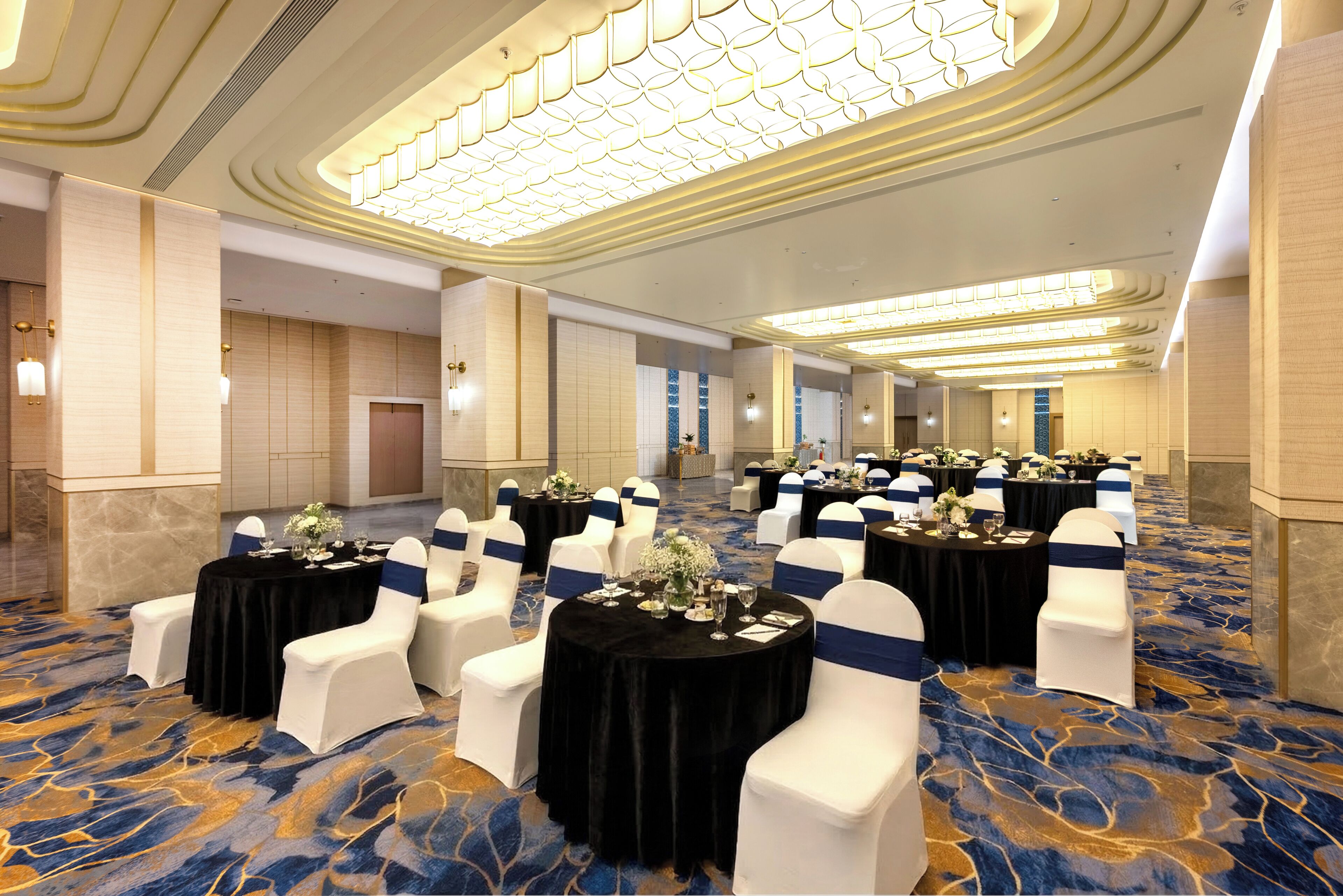 A banquet hall with round tables, white chairs, and blue sashes.