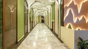 Un pasillo de hotel con piso de mármol reflectante, paredes verdes y una decoración mural con temática de montaña.