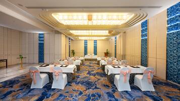 A conference room with tables set for a meeting, chairs with bows, a patterned carpet, and a decorative ceiling light fixture.