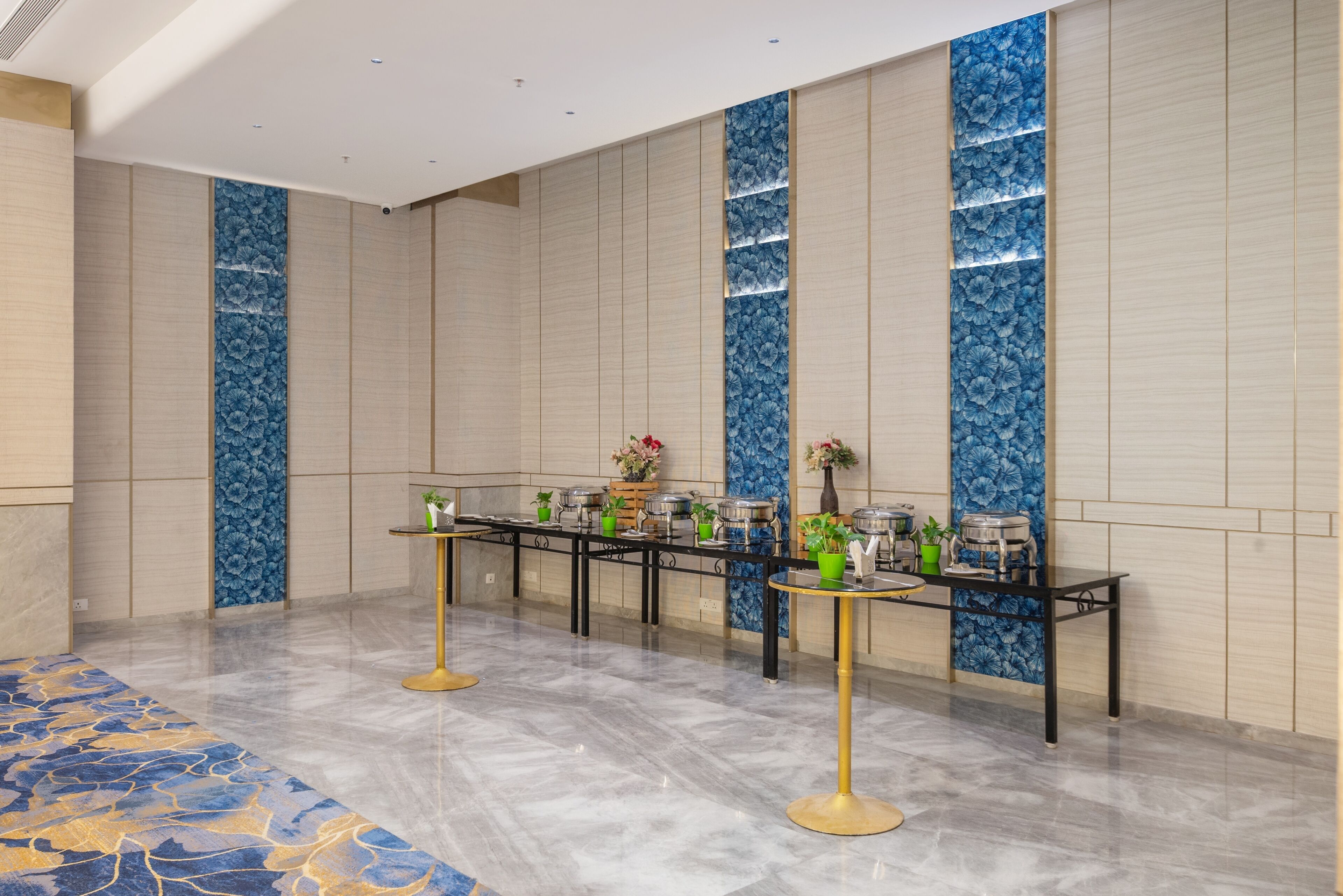 A modern hotel lobby with a long reception table, potted plants, and a patterned carpet.