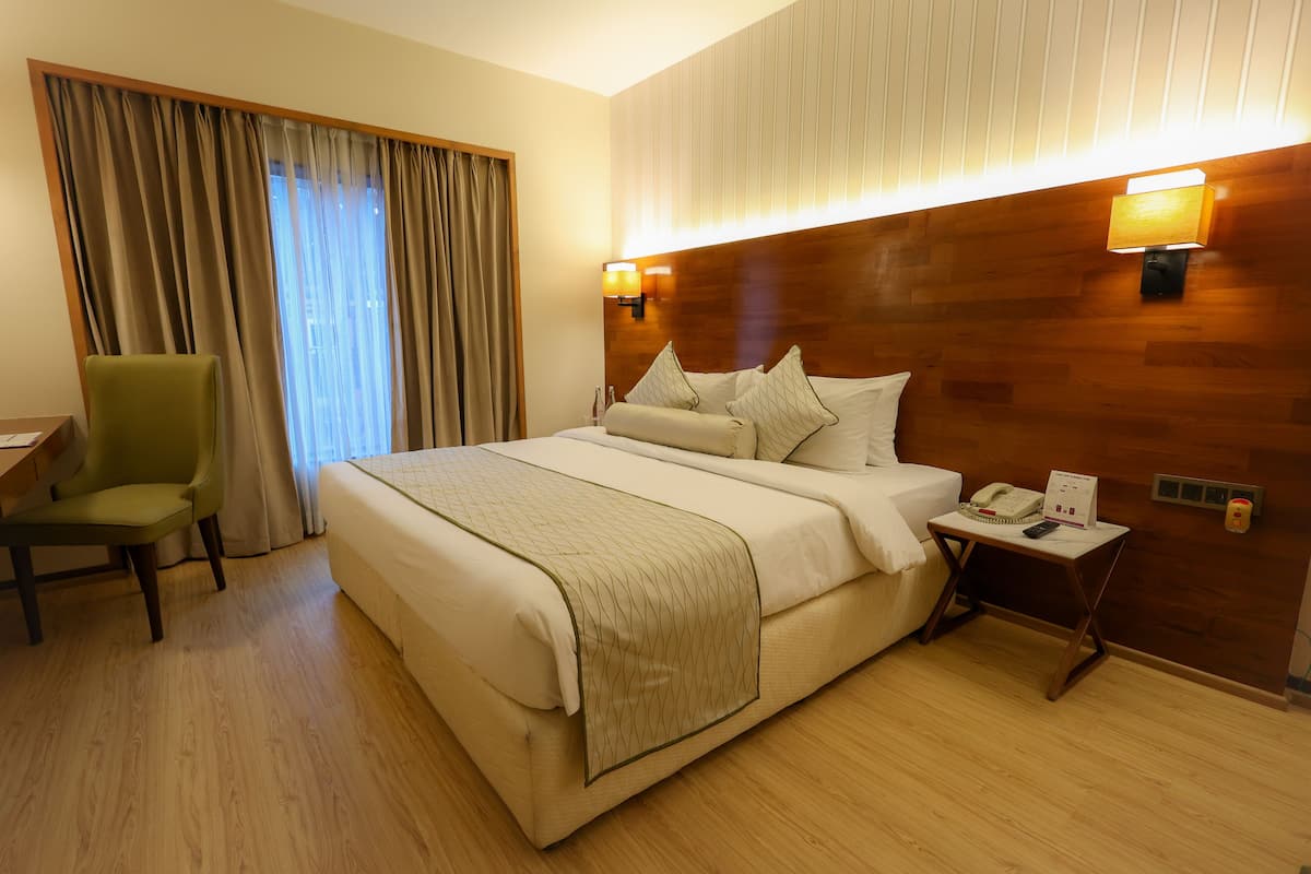 Habitación de hotel con una cama grande, un escritorio, una silla y una mesita de noche con teléfono y cartel.