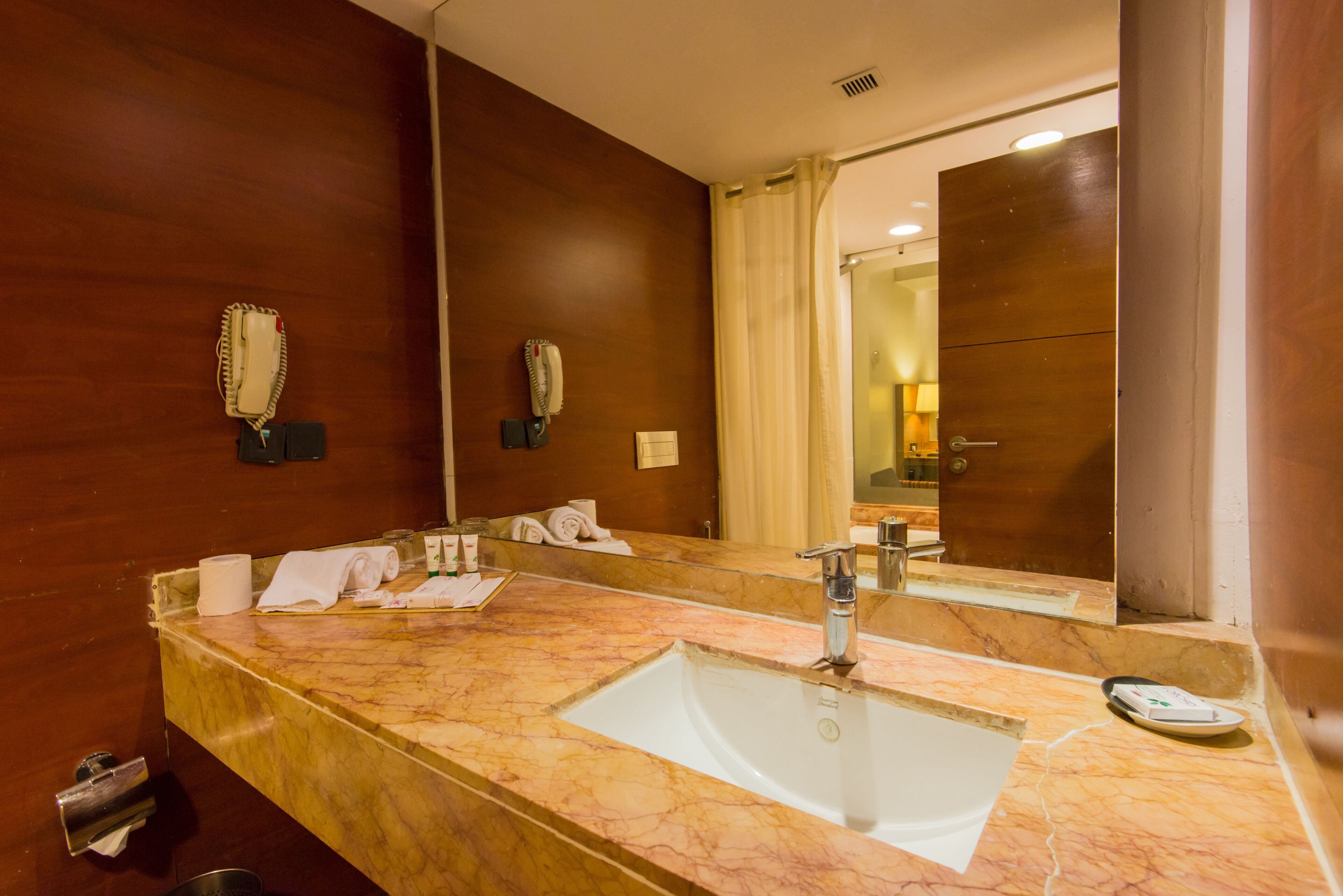 A hotel bathroom with a marble sink, two hair dryers, a towel rack, and a mirror.