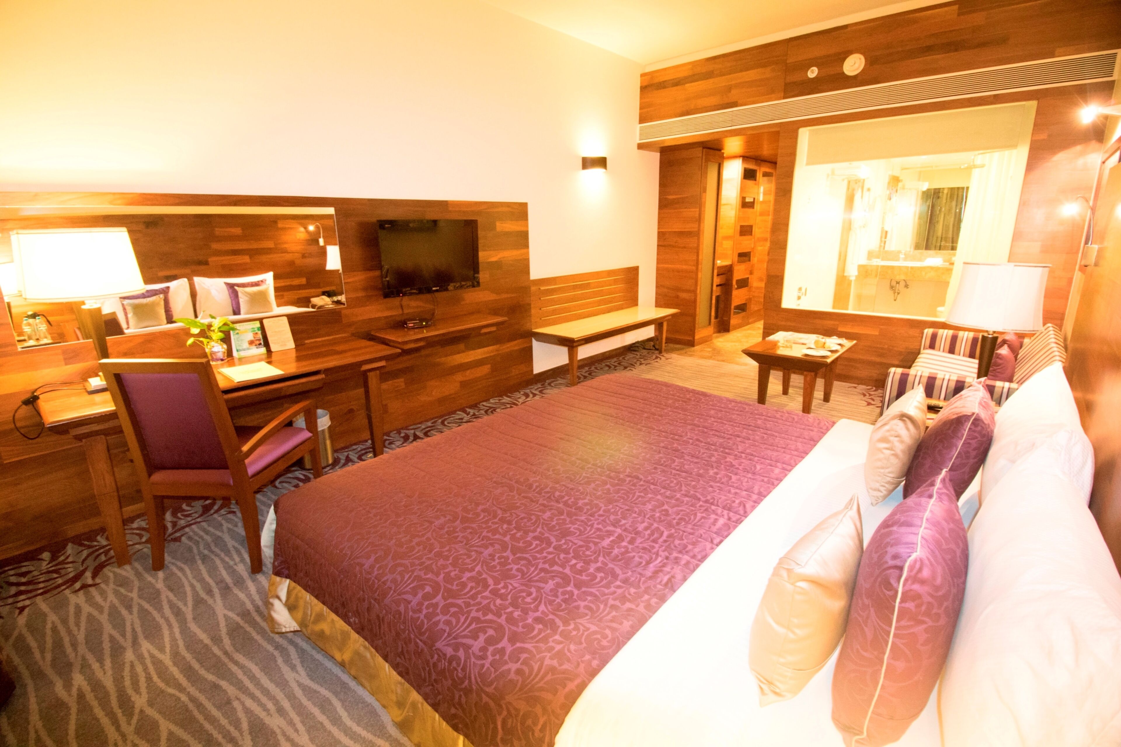 Ein Hotelzimmer mit einem großen Bett, einem Schreibtisch mit Stuhl, einem Fernseher, einem Spiegel und einem Badezimmer mit Dusche und Toilette.