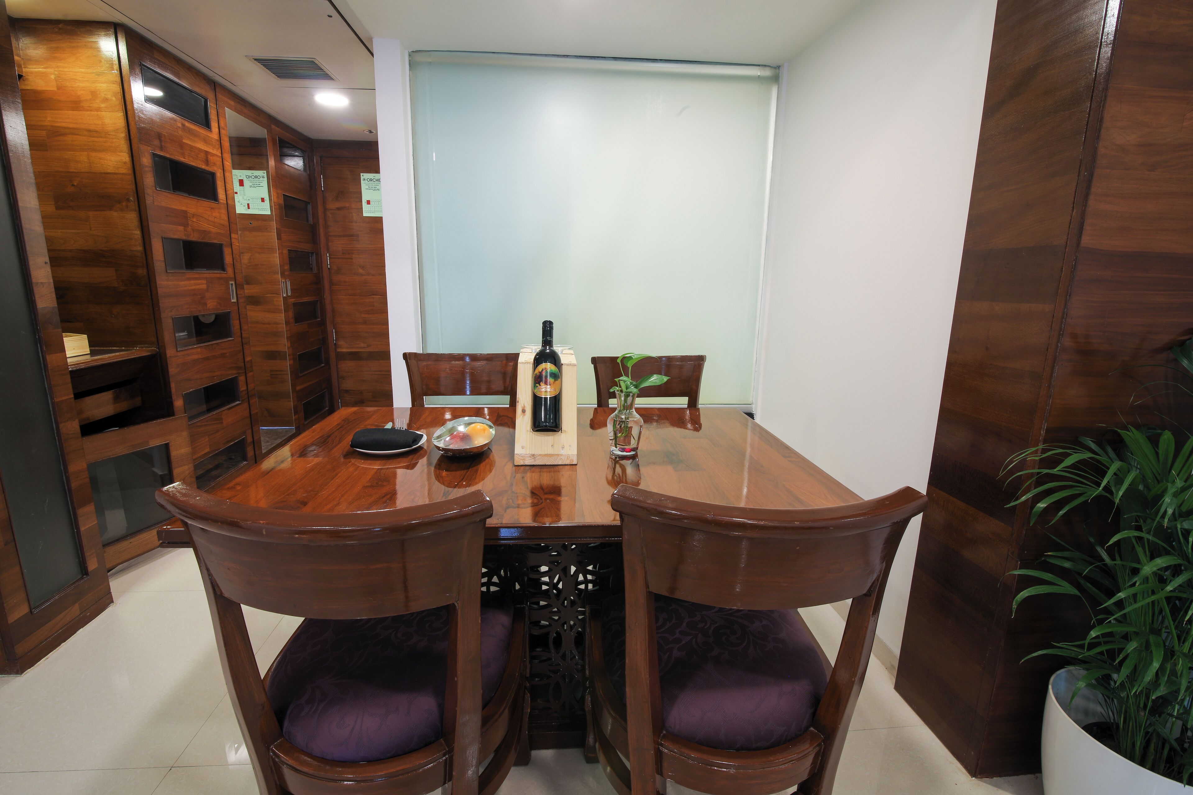 A wooden dining table with chairs, a bottle of wine, and a small plant.
