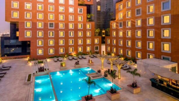 Un patio de hotel con piscina, sillones de descanso y un edificio moderno con múltiples ventanales.