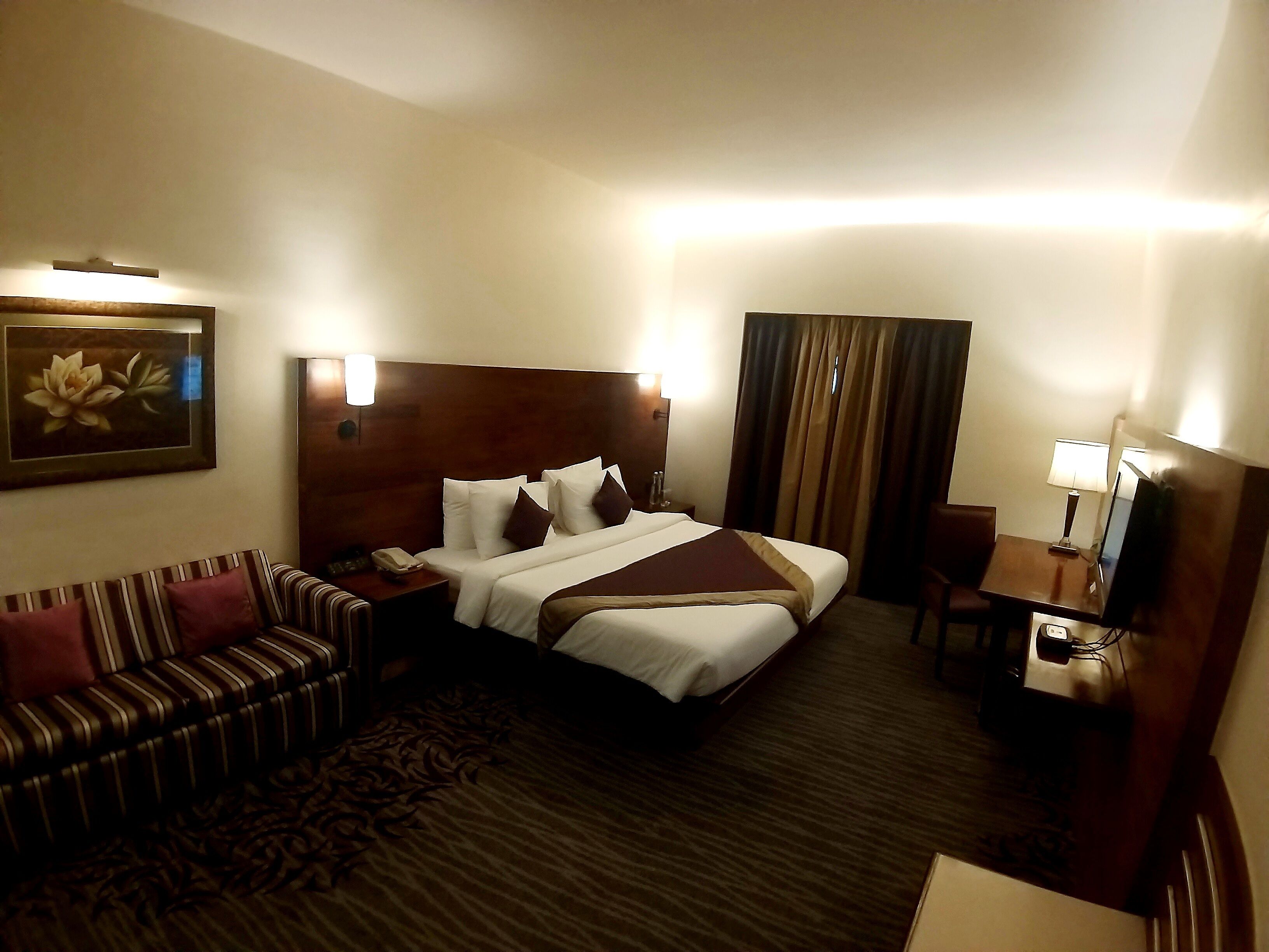 Une chambre d’hôtel avec un grand lit, un canapé, un bureau avec une lampe et un tableau au mur.
