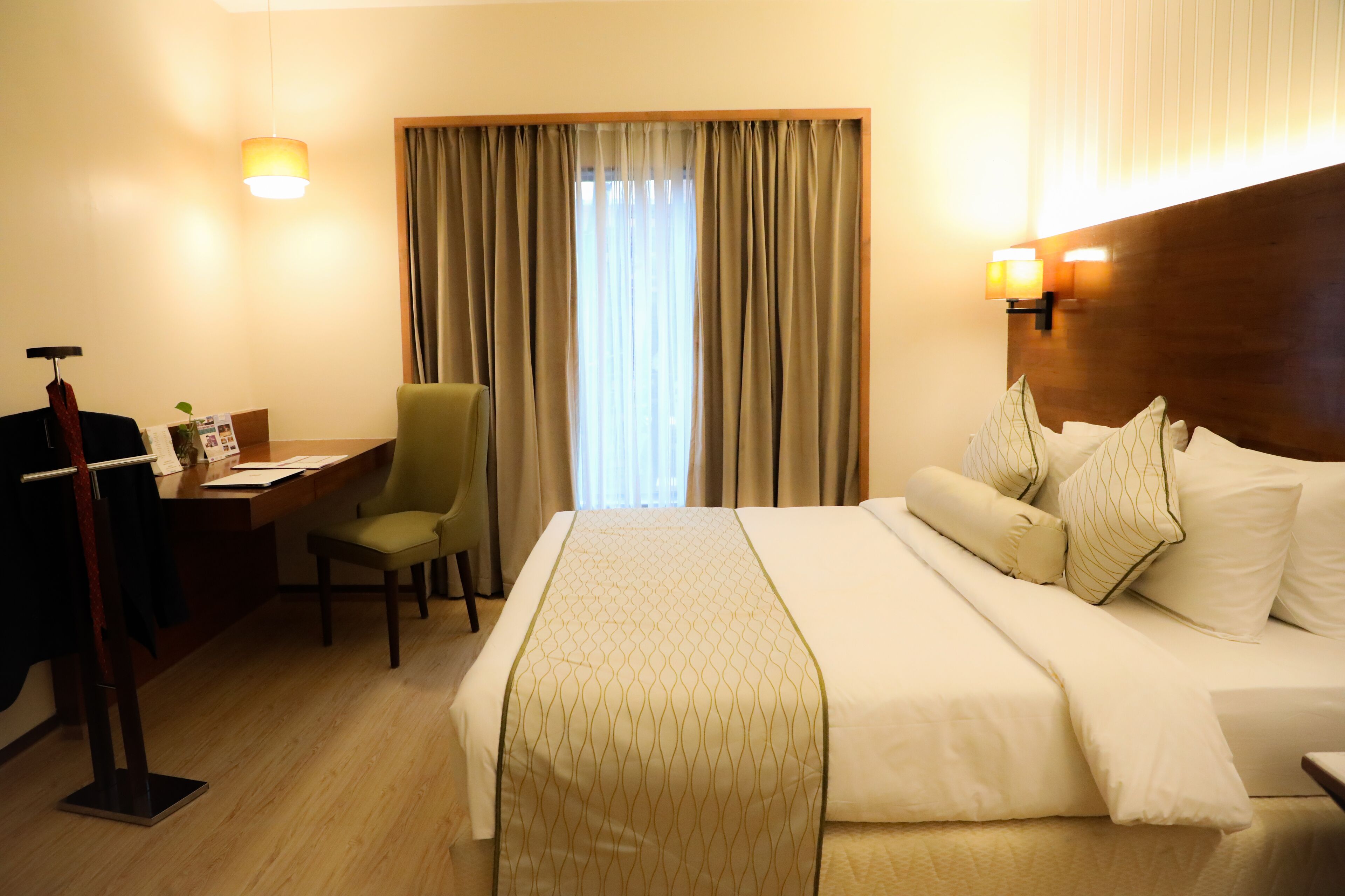 Una habitación de hotel con cama, escritorio, silla y ventana con cortinas.