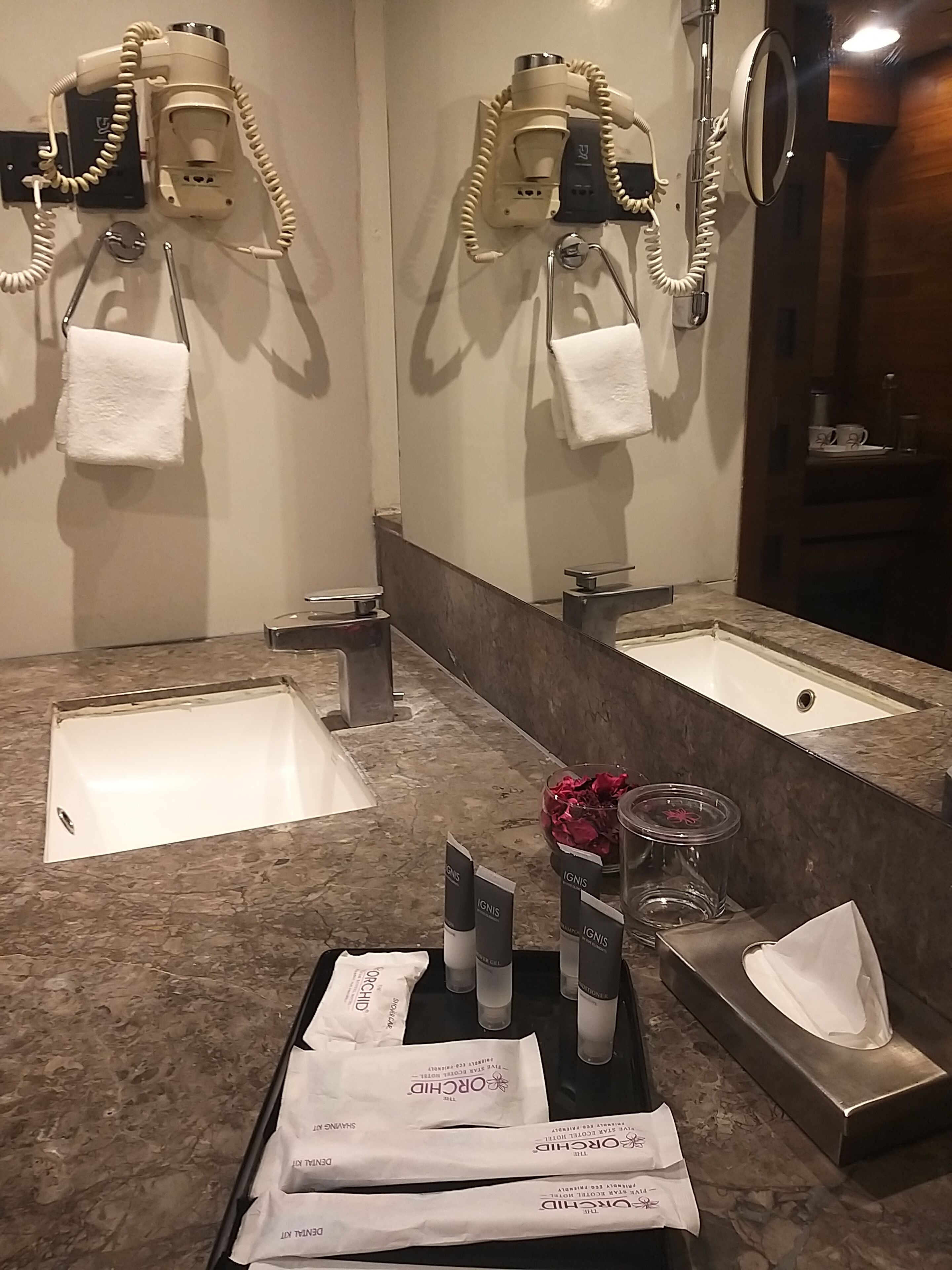A bathroom with two sinks, a mirror, and a towel rack. There are toiletries on the counter.