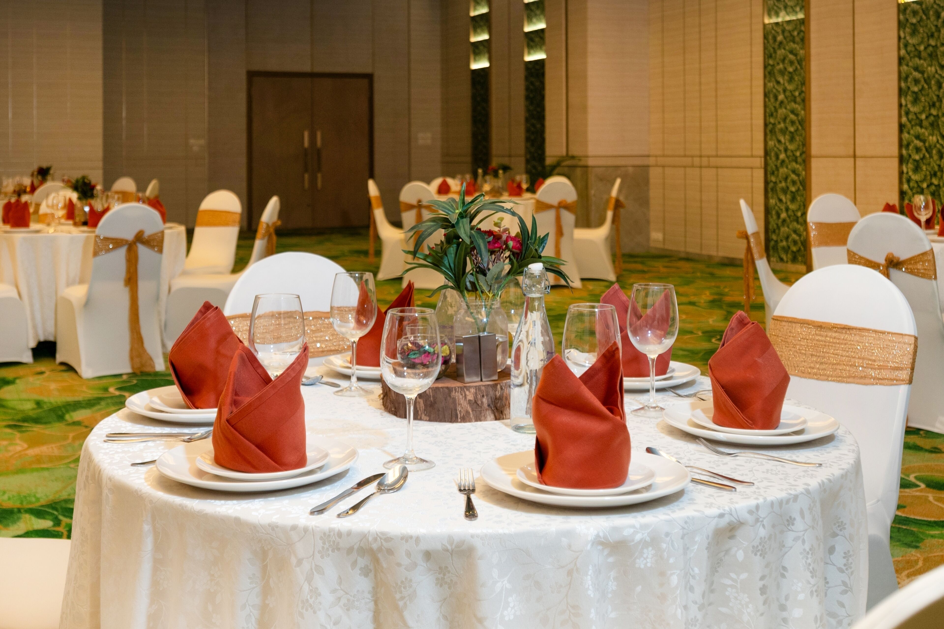A round table set for a formal event with white chairs, a floral centerpiece, and red napkins.