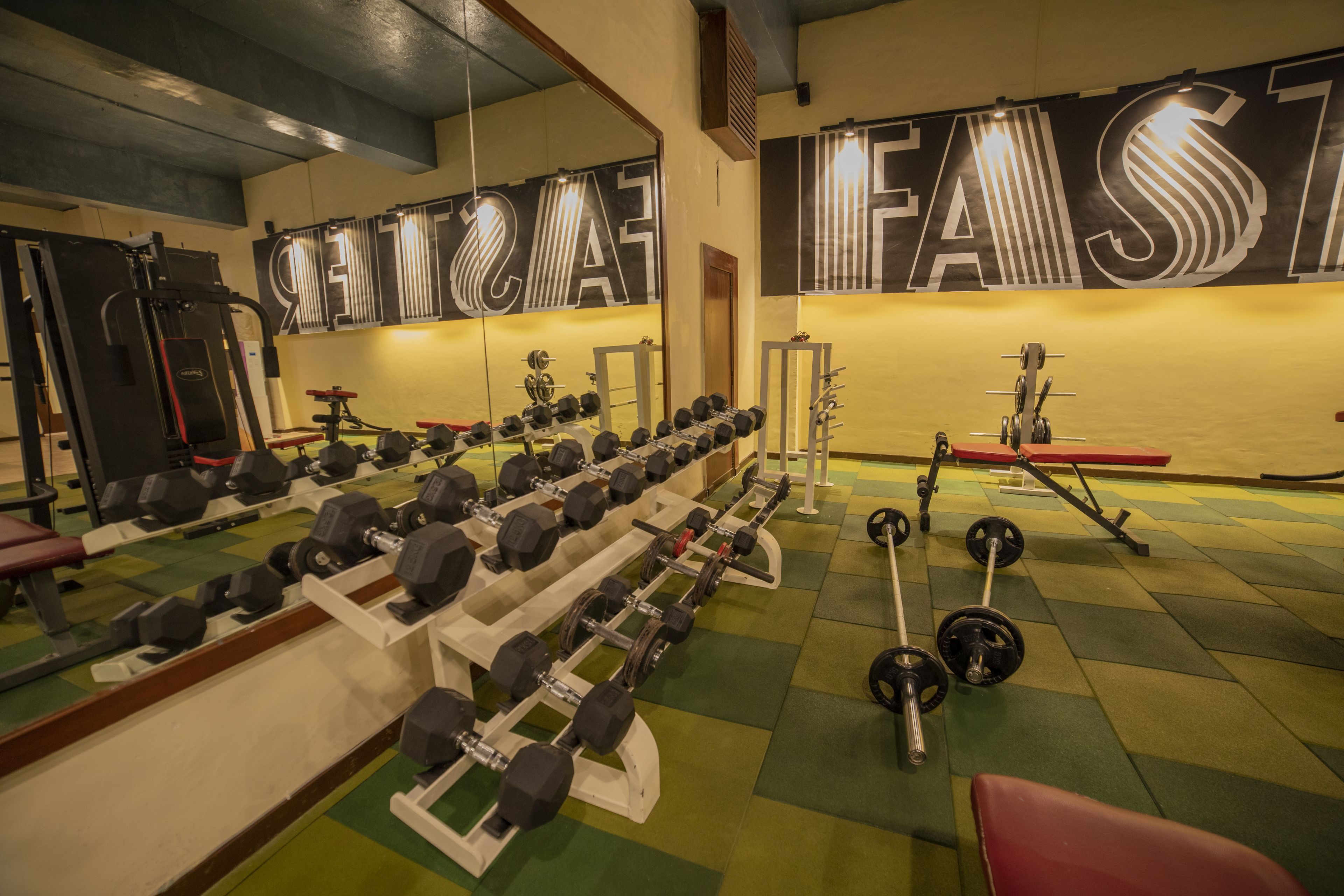 A gym with weightlifting equipment, mirrors, and a large motivational sign on the wall.