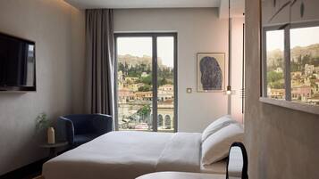 Habitación de hotel con cama, una silla, televisor, un cuadro y vista panorámica de la ciudad.