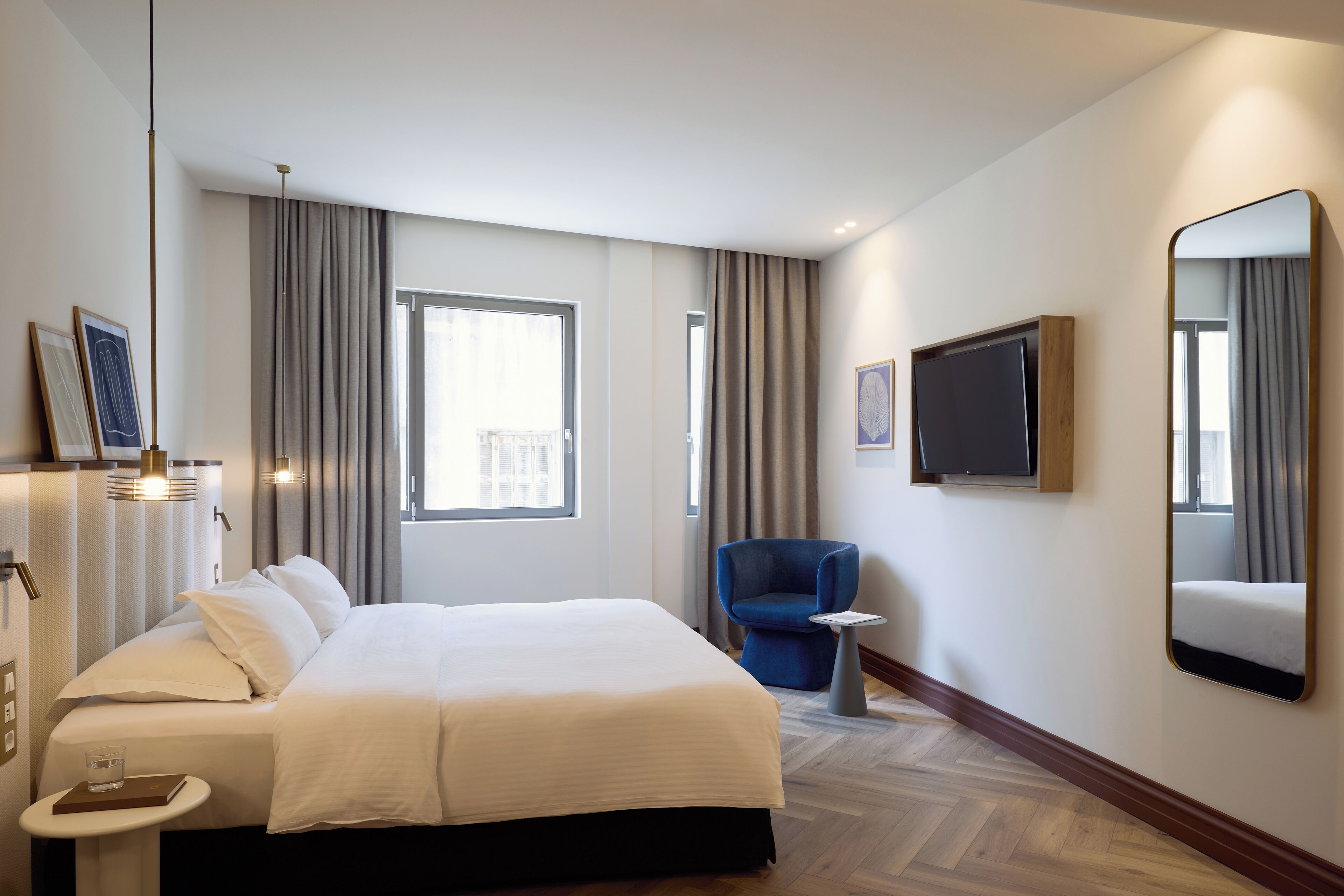 A hotel room with a large bed, a small table, a chair, a TV, and a large mirror.