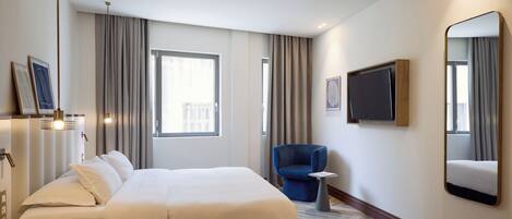 A hotel room with a large bed, a small table, a chair, a TV, and a large mirror.
